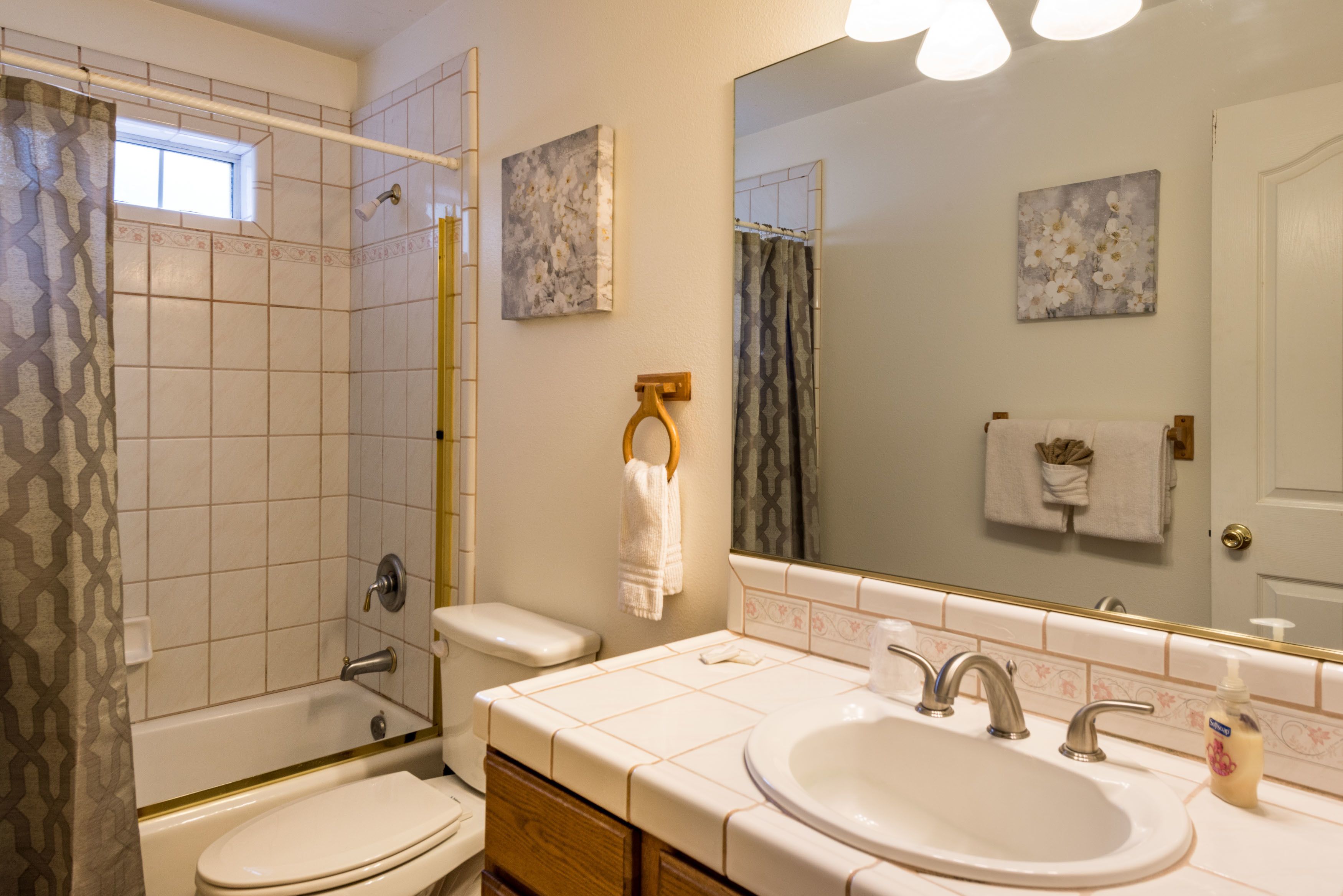 Un baño con bañera, inodoro y lavamanos. Hay toallas colgadas en ganchos y una cortina de ducha.