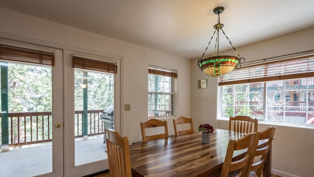 A dining area with a wooden table and chairs, large windows with blinds, and a hanging light fixture. - Inside Yosemite Lower Cascades (Yosemite National Park)