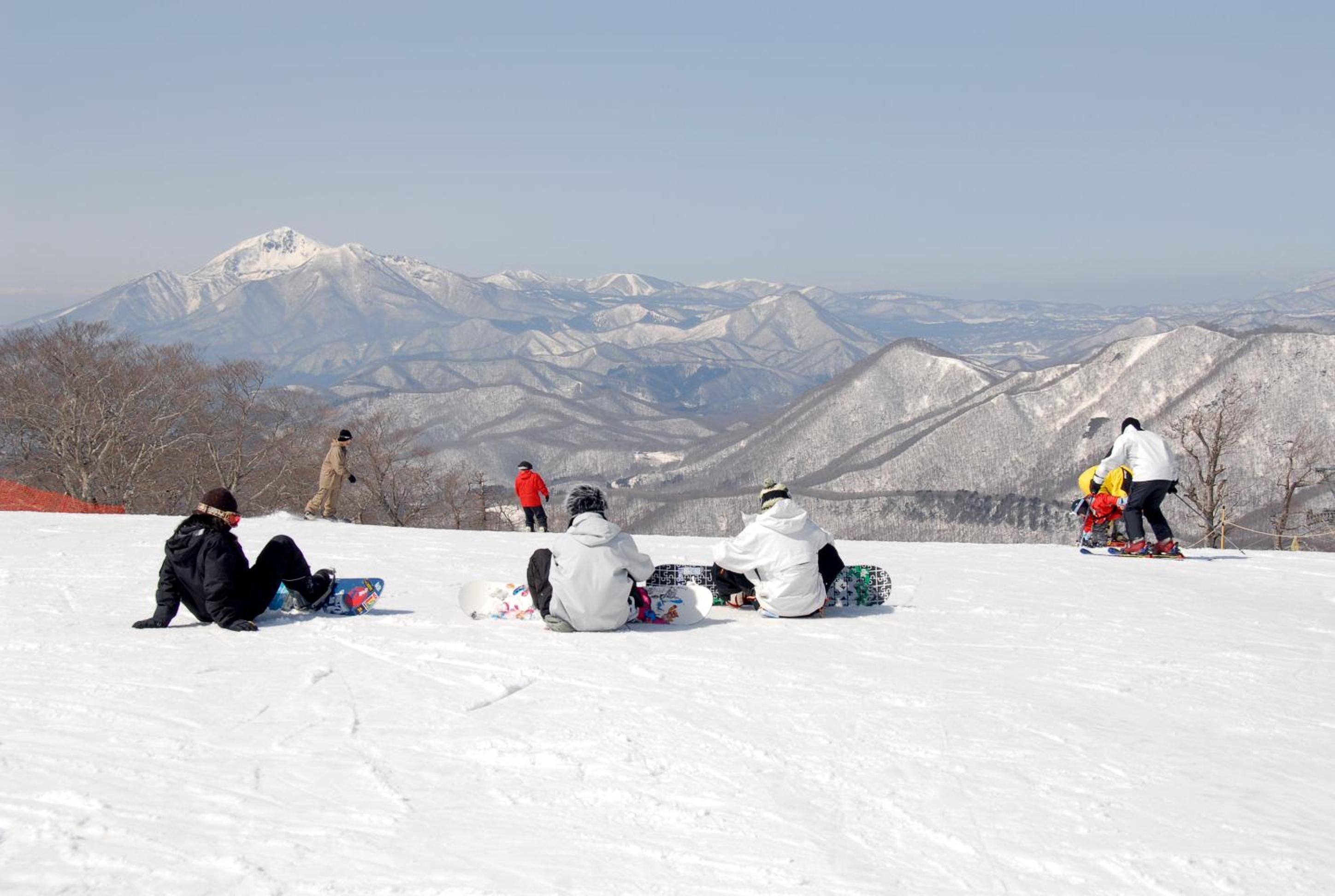 A group of people sitting on a snow-covered slope with a mountain range in the background.