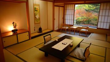 A traditional Japanese room with tatami flooring, a low table with a placemat, and a view of autumn foliage through a shoji screen.