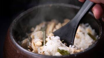 A close-up of a hand stirring rice with a black spoon in a dark-colored pot.