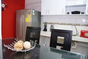 A kitchen with white cabinets, a stainless steel refrigerator, a glass table with a bowl of snacks, and a red wall.