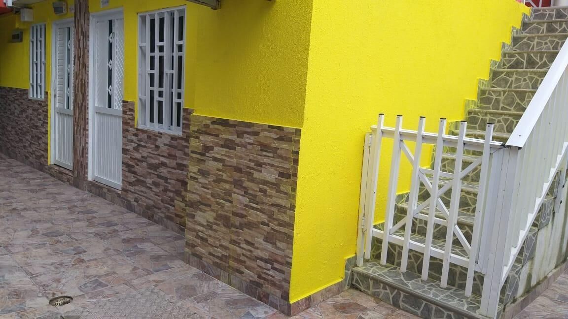 Un edificio con fachada amarilla, una escalera de piedra y una verja blanca.