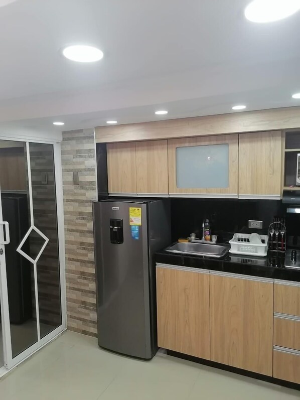 A modern kitchen with a stainless steel refrigerator, wooden cabinets, a black countertop, and a glass door pantry.