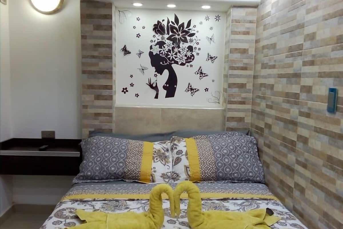 A hotel room with a bed featuring a decorative headboard with a floral and butterfly design, a bedside table, and patterned bedding.