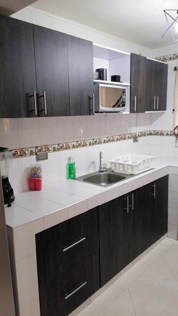 A kitchen with dark wooden cabinets, white countertops, a stainless steel sink, and a microwave. - Posada Amiel Forbes (San Andrés)