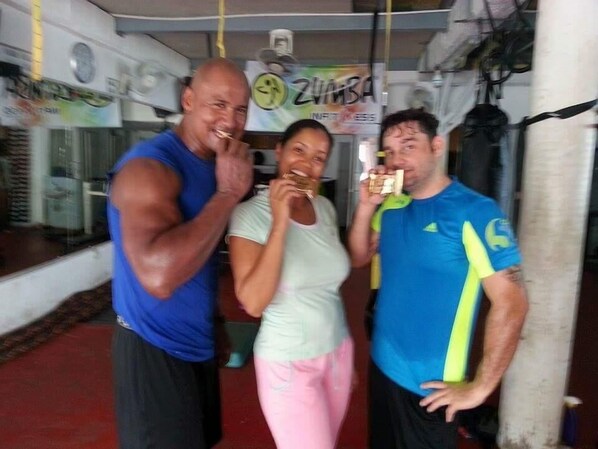Tres personas en un gimnasio con equipo de ejercicio y un letrero que dice "Zumba".