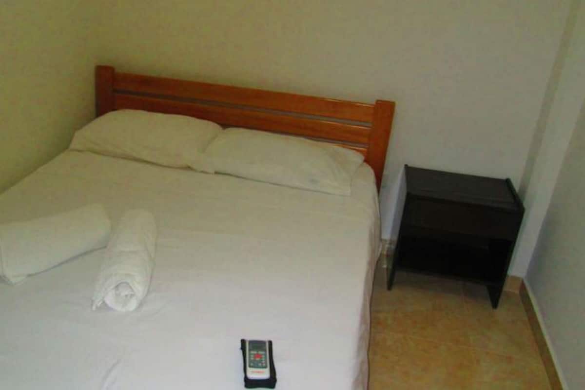 A bed with a wooden headboard, white linens, and a rolled towel. A remote control is on the bed.