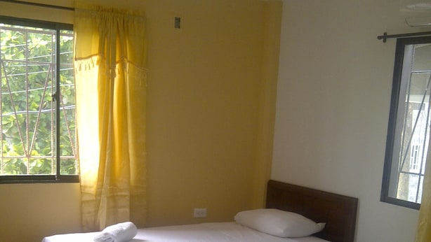 A room with two beds, a window with yellow curtains, and a view of greenery outside. - Posada Infitness 2 (San Andrés)
