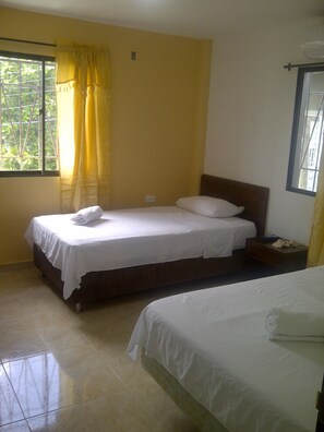 Habitación con dos camas, una ventana con cortinas amarillas y vistas al verdor exterior.