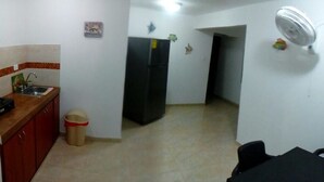 A kitchen with a sink, a refrigerator, and a trash bin. There is a dining table with chairs and a ceiling fan. - Posada Infitness 2 (San Andrés)
