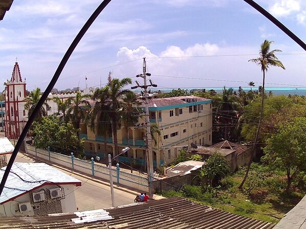 A multi-story building with a flat roof, surrounded by greenery and a church with a cross on top. - Sweet Sand Hostel (Isla de San Andres)