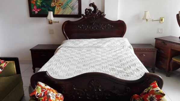 A bedroom with a wooden bed, a nightstand, a dresser, and a wall-mounted lamp.