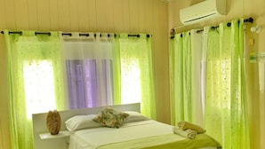 Un dormitorio con cama, mesita de noche, aire acondicionado instalado en la pared y una ventana con cortinas verdes.