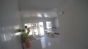 Una habitación amplia con un gran ventanal, un sofá blanco, una mesita y un jarrón con flores.