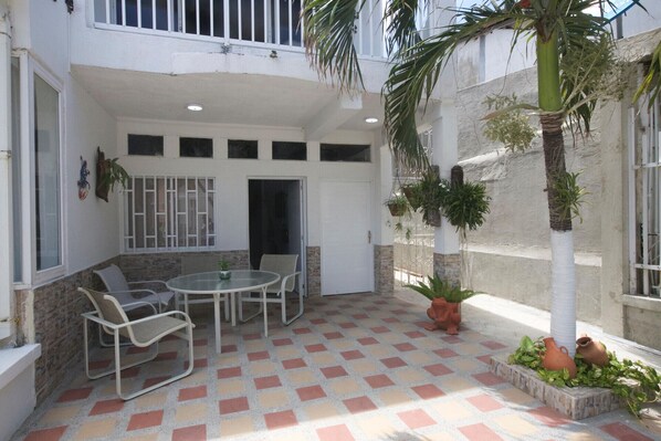 A covered patio area with a tiled floor, a round table with chairs, and potted plants.