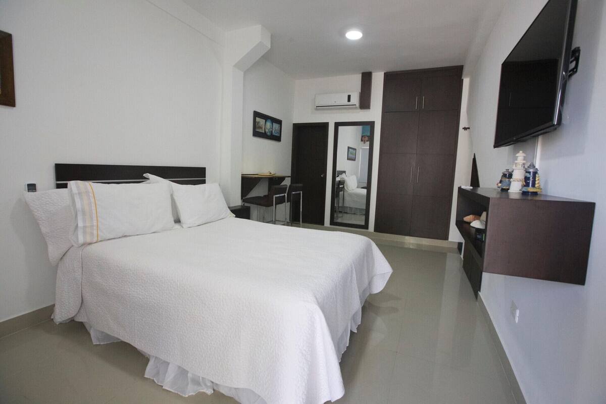 A hotel room with a large bed, a desk, a wardrobe, and a television on the wall.