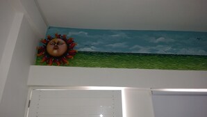A room with a mural of a sun and birds, a white door, and a green landscape. - Hospedaje Solymar I Sarie Bay (San Andrés)