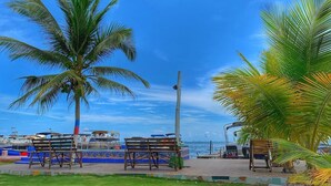 A beachside area with a palm tree, benches, and a view of boats in the background. - Posada Donde Pilo Avila (San Andrés)