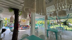 Un espace de restauration en plein air agrémenté de décorations en macramé suspendues, de tables et de chaises blanches et turquoise.