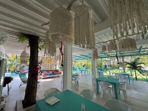 Een terras met hangende macramé decoraties, witte en turquoise tafels en stoelen.
