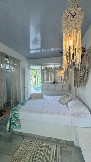 Een ruime slaapkamer met een groot bed, macramé decoratie aan de muur en uitzicht op groen.