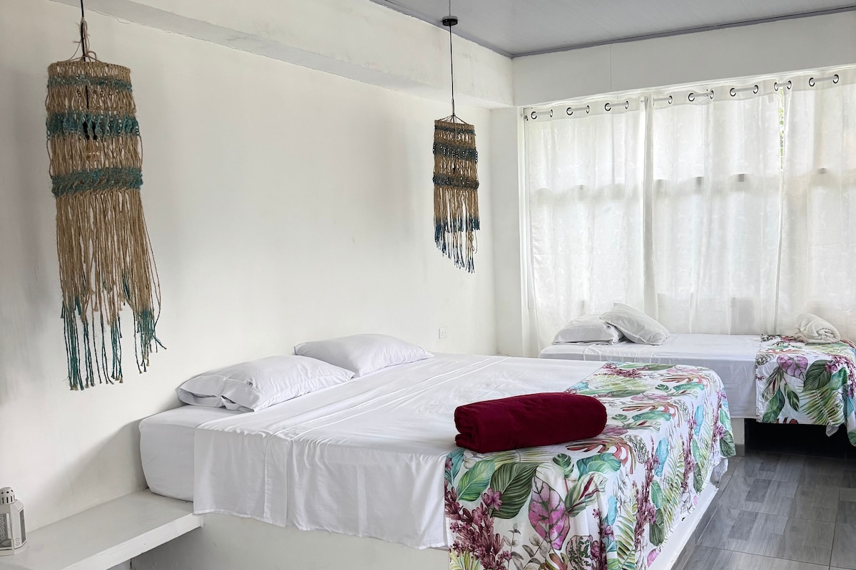 Un dormitorio moderno con una cama grande, una cama más pequeña, un banco y una lámpara colgante.