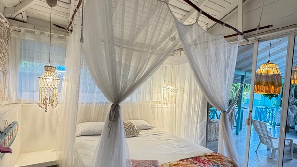 Un dormitorio con cama con dosel, una mesita de noche pequeña y vistas al exterior a través de un ventanal.