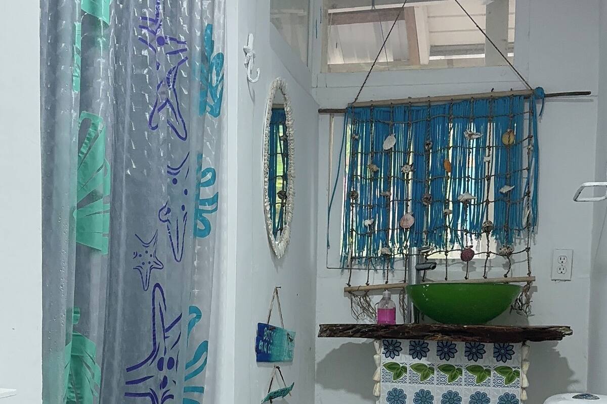 Une salle de bain comprenant des toilettes, un lavabo avec un récipient décoratif, un rideau de douche orné de motifs d’étoiles de mer, un tapis bleu et un filet bleu suspendu.