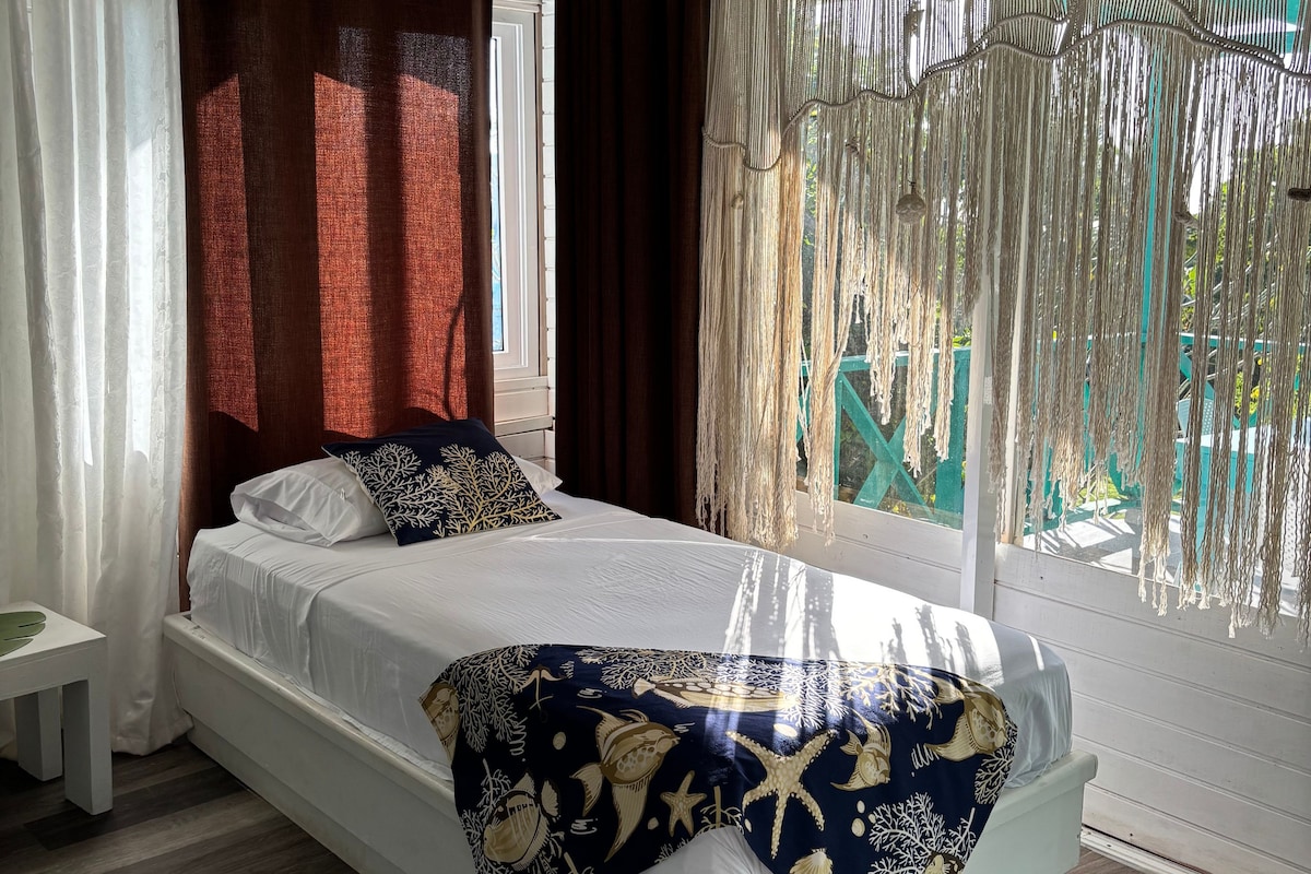 Un dormitorio con cama blanca, cortinas oscuras y vistas al exterior.