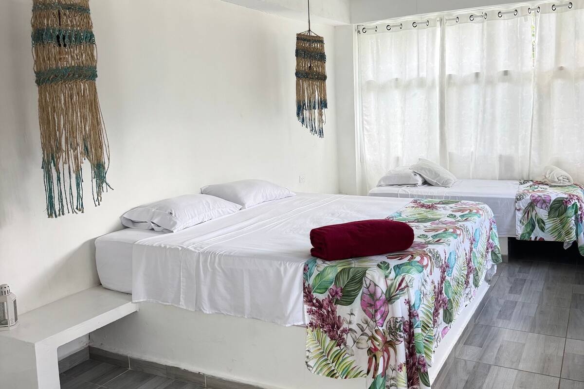 Une chambre moderne avec un grand lit, un plus petit lit, un banc et un luminaire suspendu.