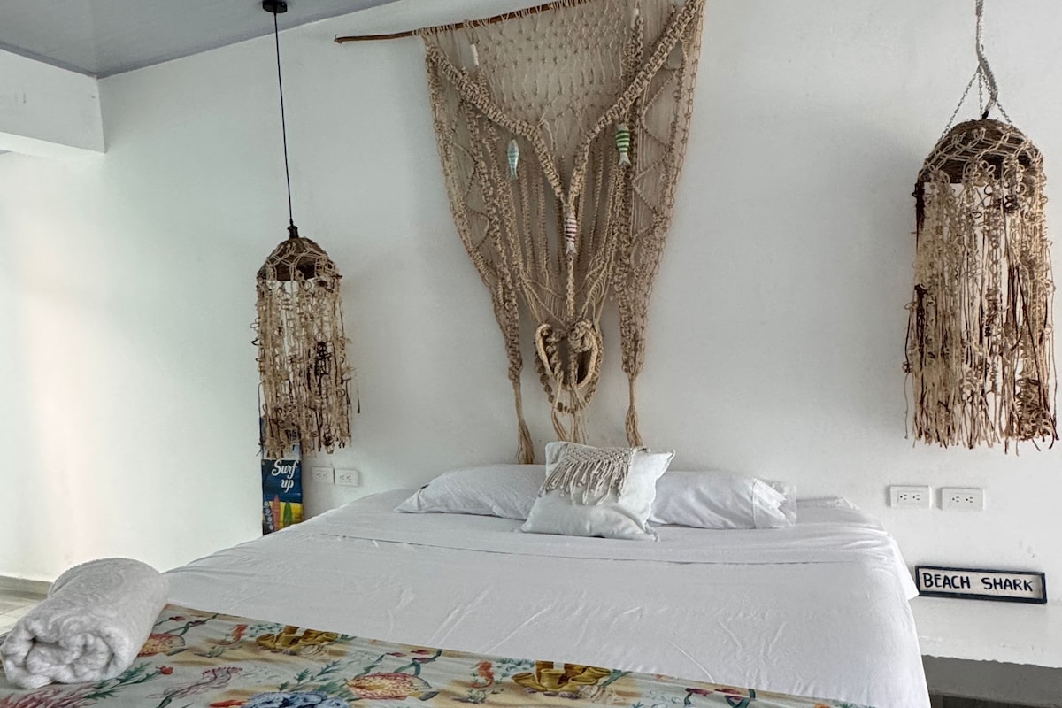 Un dormitorio con una cama, un tapiz de macramé en la pared y dos lámparas de macramé.