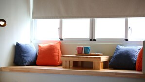 Un dormitorio con un asiento junto a la ventana, almohadas y una mesita.