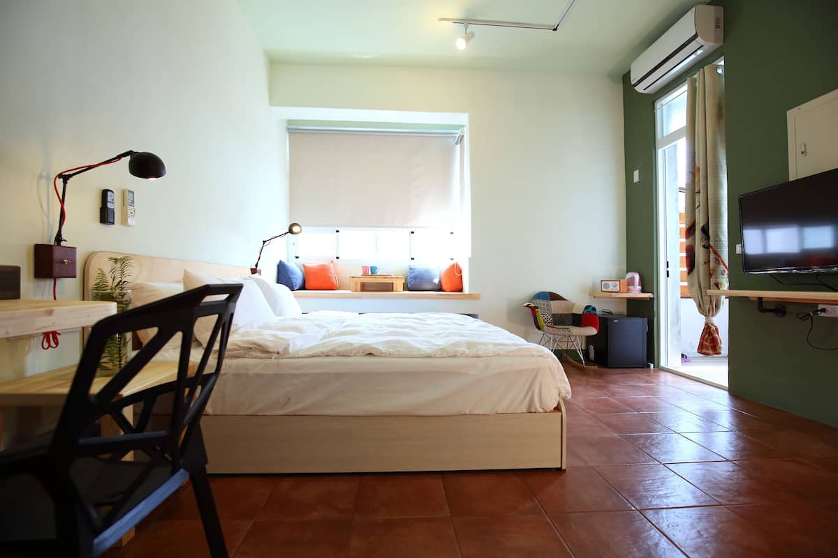 A bedroom with a bed, a desk, a chair, a TV, and a window with a view.