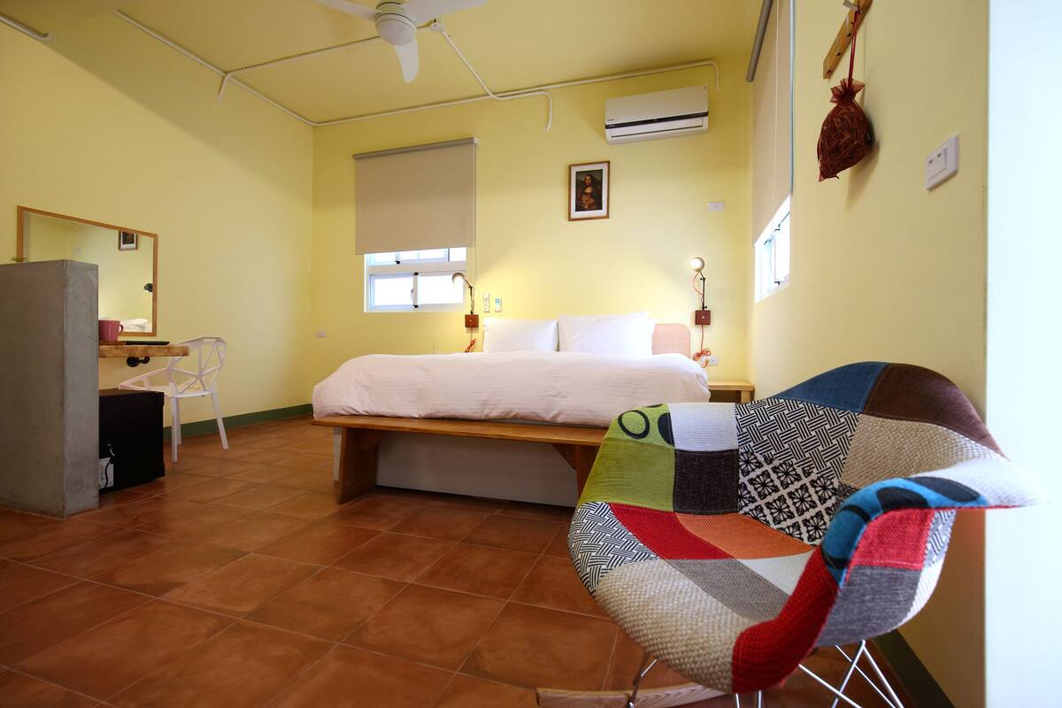 A bedroom with a bed, a chair, a desk, and a window.
