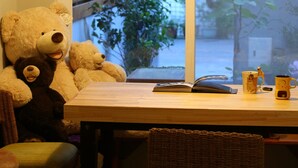 Un rincón comedor con un gran oso de peluche, una mesa con un libro y tazas, y una silla de mimbre.