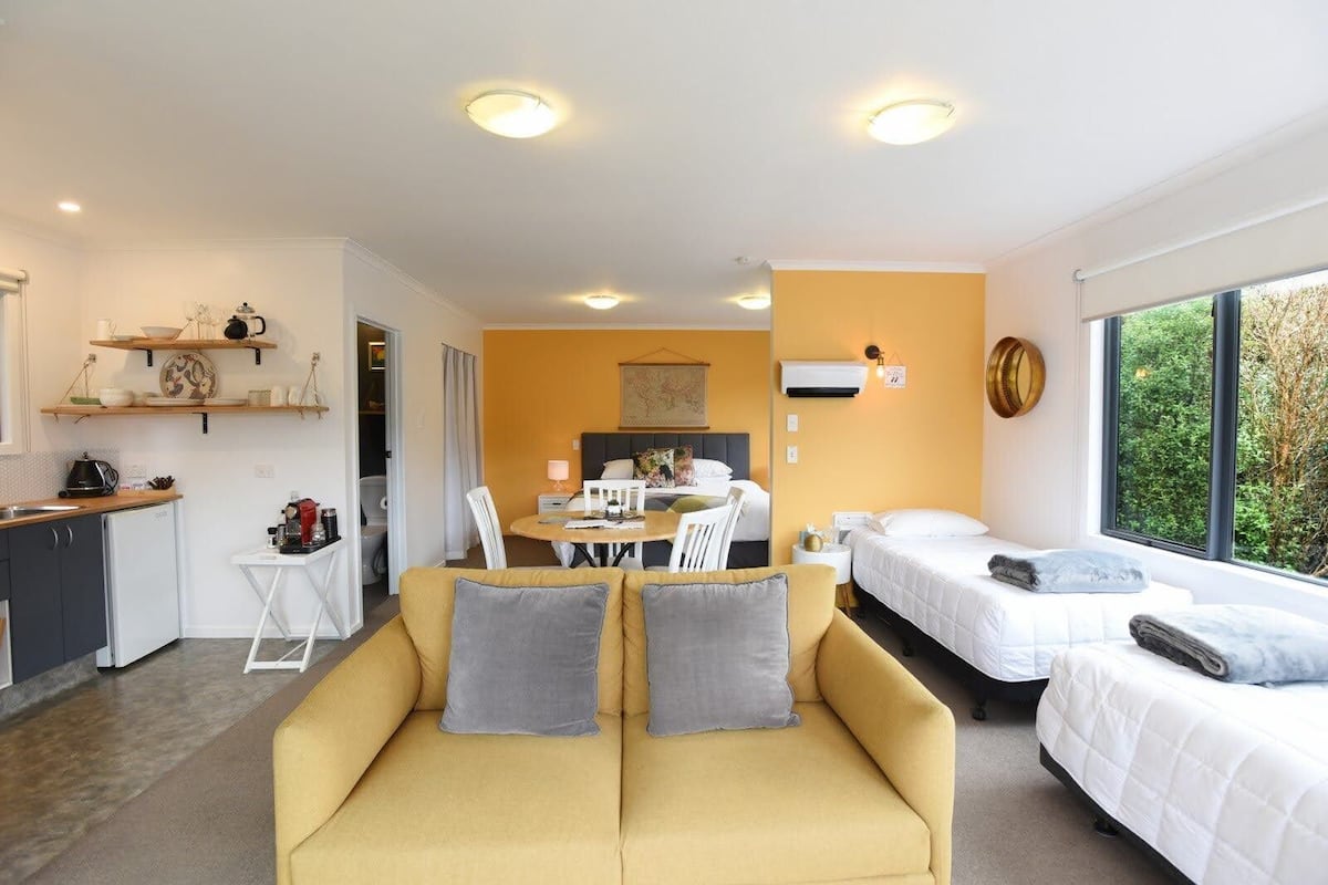 A modern hotel room with a yellow sofa, a bed, a dining area, and a kitchen.