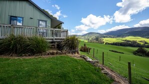A large, single-story building with a balcony, surrounded by a well-maintained lawn and a scenic view of rolling hills and mountains. - Mohua Park - Catlins Eco Accommodation (Tawanui)