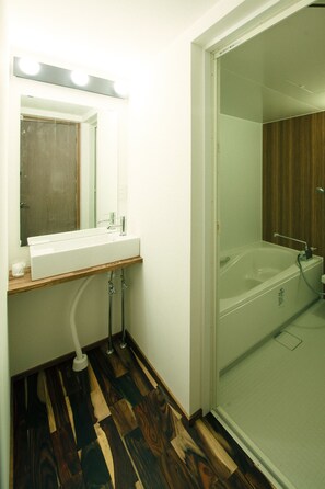 A bathroom with a wooden vanity, a sink, a mirror with lights, and a glass-enclosed shower area. - Anchor Site (Takayama)
