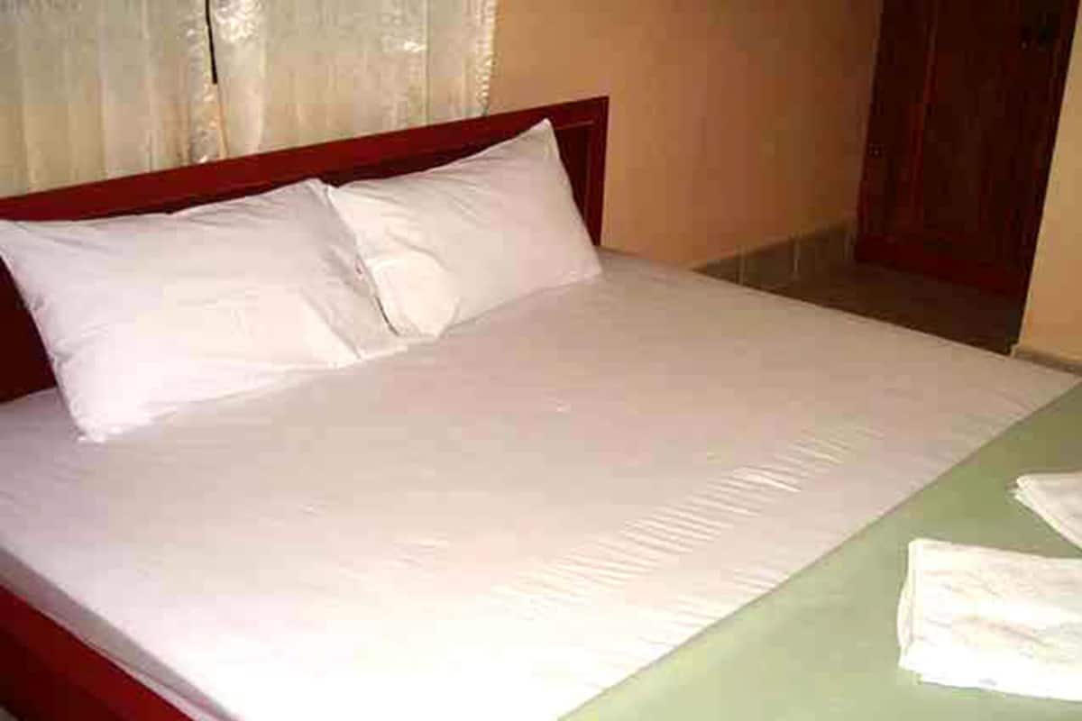 A bed with white linens and a green bedspread, a wooden headboard, and a door in the background.