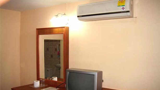 A hotel room with a wooden desk, a computer monitor, a mirror, and an air conditioning unit.