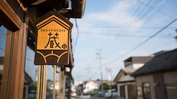 A wooden sign with "GUESTHOUSE" and Japanese characters, indicating a guesthouse on a street with buildings and power lines.
