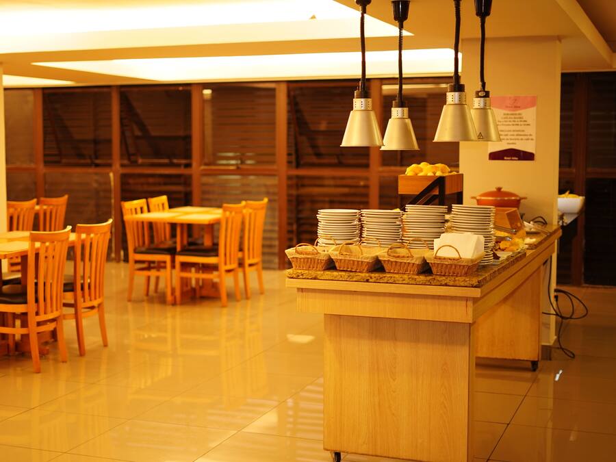 A dining area with wooden tables and chairs, a buffet counter with stacked plates and baskets, and hanging pendant lights.