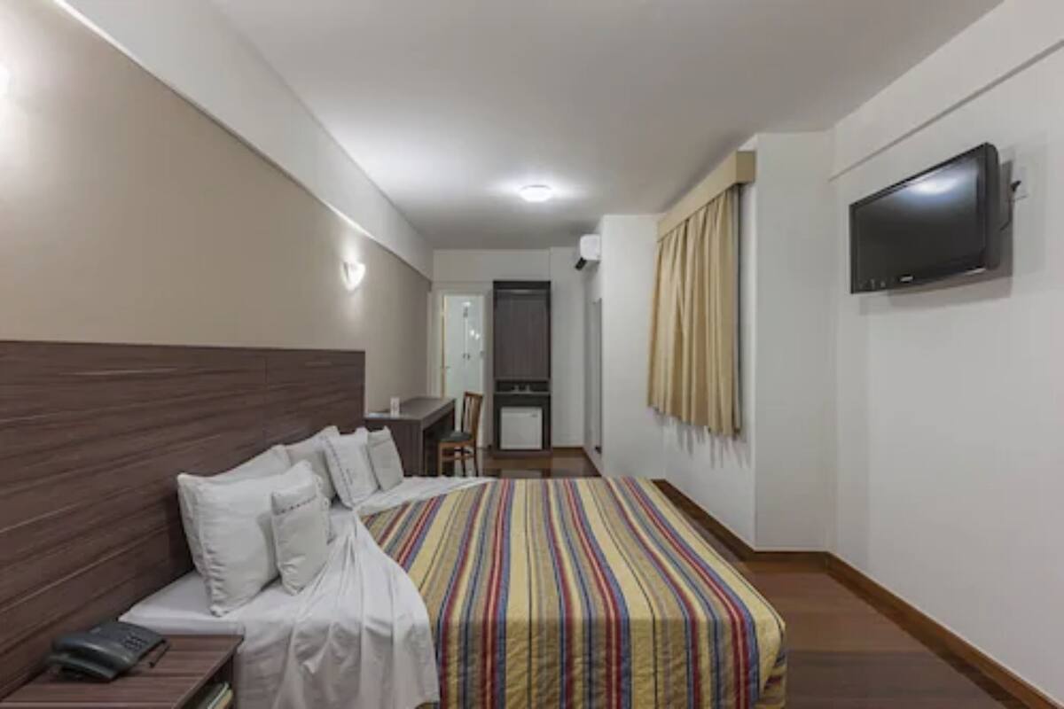 A hotel room with a bed, bedside table, TV, and a desk with a chair.