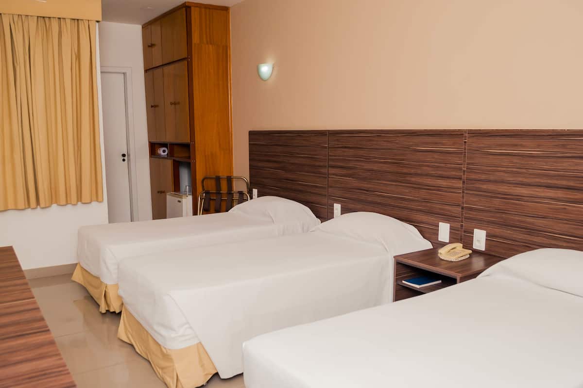 A hotel room with two single beds, a wooden headboard, a bedside table with a phone and a lamp, and a wardrobe with a mirror.
