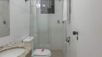 A compact bathroom with a granite sink, white toilet, and a glass shower enclosure.