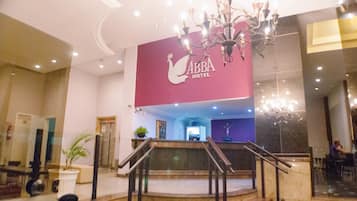 A hotel lobby with a grand staircase, a chandelier, and a sign for the Abba Hotel.
