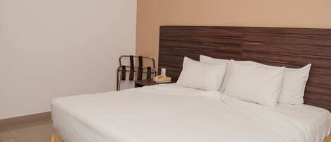 A neatly made bed with white linens, a wooden headboard, and a bedside table with a lamp and a telephone.