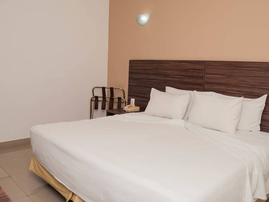 Una cama bien hecha con sábanas blancas, un cabecero de madera y una mesita de noche con una lámpara y un teléfono.