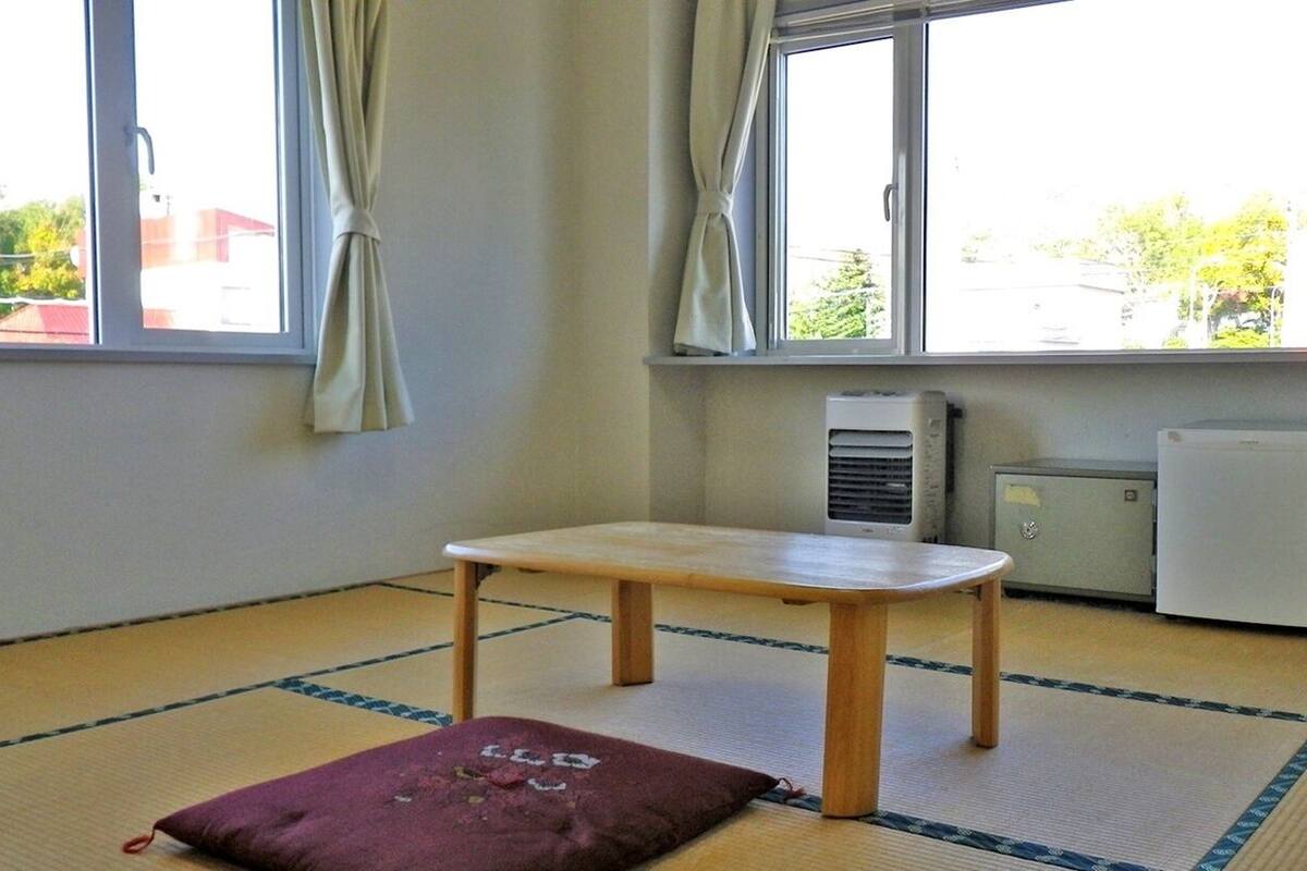 A room with tatami flooring, a small wooden table, a cushion, and a window with curtains.